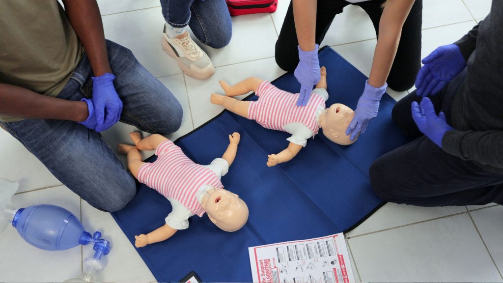two small dummies are on the floor while a person demonstrates CPR